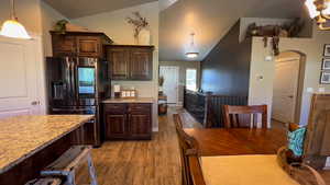 Kitchen featuring stainless steel fridge with ice dispenser, dark brown cabinets, dark wood-type flooring, hanging light fixtures, and arched walkways