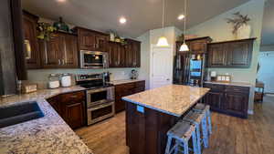 Kitchen featuring dark brown cabinets, appliances with stainless steel finishes, dark wood-type flooring, hanging light fixtures, and a center island