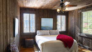 Bedroom featuring wood walls, dark wood finished floors, wooden ceiling, multiple windows, and ceiling fan