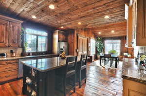 Kitchen with dark stone counters, wood ceiling, dark wood-type flooring, appliances with stainless steel finishes, and a breakfast bar area