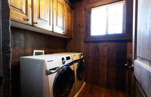 Laundry area with wooden walls, dark wood-style floors, cabinet space, and independent washer and dryer