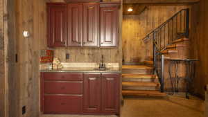 Bar area featuring wooden walls, stairway, light colored carpet, light stone counters, and brown cabinets