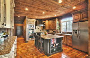 Kitchen featuring stainless steel appliances, wood ceiling, dark wood-type flooring, light stone countertops, and premium range hood