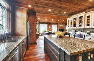 Kitchen featuring glass insert cabinets, wood ceiling, light stone countertops, dark wood-type flooring, and stainless steel appliances