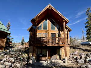 Back of house featuring log exterior, a wooden deck, and a patio