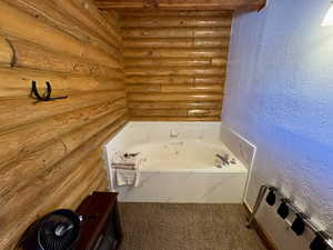 Bathroom with a textured wall, a garden tub, log walls, and carpet