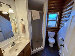 Bathroom featuring a shower stall, vanity, dark tile patterned flooring, a textured wall, and rustic walls