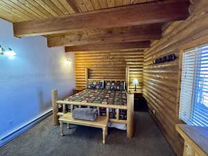 Bedroom with a textured wall, a baseboard heating unit, dark colored carpet, a wooden ceiling with exposed beams, and rustic walls
