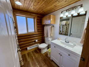 Full bathroom featuring a textured wall, a shower with curtain, vanity, dark wood-style floors, and a baseboard heating unit