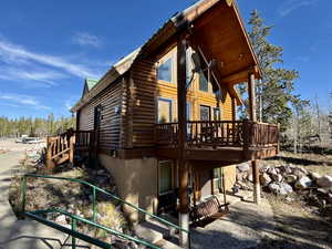 View of side of property featuring log siding, a wooden deck, and a patio