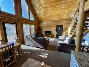 Carpeted living area with high vaulted ceiling, log walls, wooden ceiling, and a wood stove