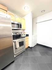 Kitchen featuring appliances with stainless steel finishes, light brown cabinetry, dark tile patterned floors, dark countertops, and washer / clothes dryer
