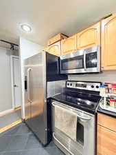 Kitchen featuring appliances with stainless steel finishes, dark tile patterned flooring, light brown cabinets, and dark countertops