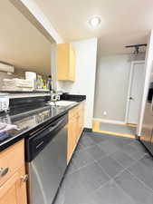 Kitchen with appliances with stainless steel finishes, light brown cabinets, dark tile patterned flooring, and dark stone counters