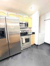 Kitchen featuring appliances with stainless steel finishes, dark countertops, dark tile patterned flooring, washer / clothes dryer, and light brown cabinets