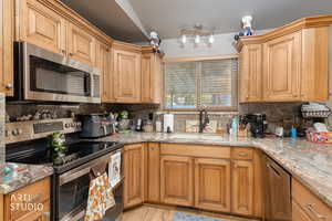 Kitchen with appliances with stainless steel finishes, light stone counters, decorative backsplash, and light wood-style flooring