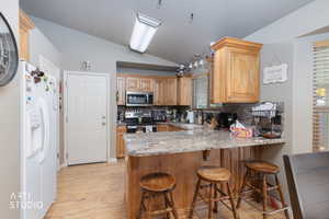 Kitchen featuring vaulted ceiling, light stone counters, tasteful backsplash, a peninsula, and light wood-style floors