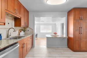 Kitchen featuring brown cabinets, light stone countertops, dishwasher, decorative backsplash, and a textured ceiling