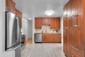 Kitchen featuring brown cabinets, appliances with stainless steel finishes, decorative backsplash, light stone counters, and a textured ceiling