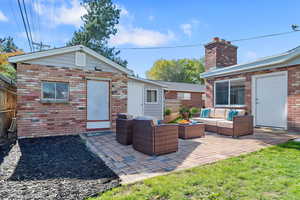 Back of property featuring brick siding, an outdoor living space, a patio, and a chimney