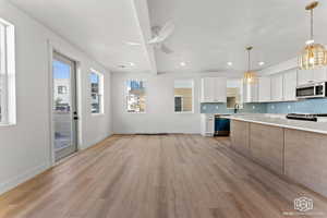 Kitchen featuring white cabinetry, tasteful backsplash, pendant lighting, light wood-style flooring, and stainless steel appliances