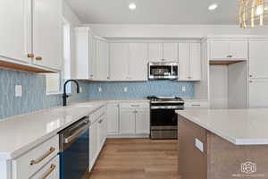 Kitchen featuring white cabinets, appliances with stainless steel finishes, light stone counters, light wood-style flooring, and recessed lighting