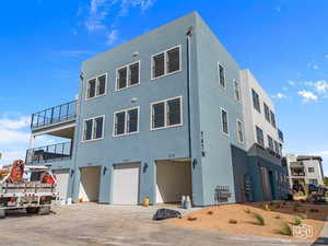 Rear view of property featuring an attached garage, stucco siding, a balcony, and driveway