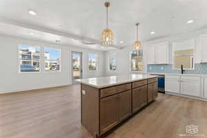 Kitchen with decorative backsplash, white cabinets, a kitchen island, light wood-style floors, and healthy amount of natural light