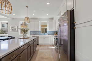 Kitchen featuring stainless steel appliances, white cabinetry, decorative light fixtures, tasteful backsplash, and light wood-style flooring