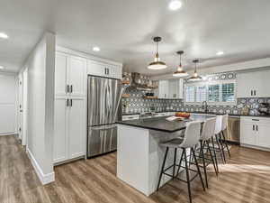 Kitchen with open shelves, white cabinetry, hanging light fixtures, stainless steel appliances, and a kitchen bar