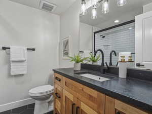 Bathroom with dark tile patterned floors, tiled shower, vanity, and recessed lighting
