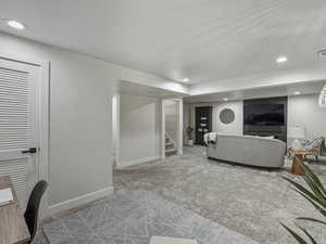 Carpeted living area with recessed lighting and stairway