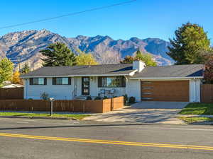 Ranch-style home with a fenced front yard, driveway, a mountain view, brick siding, and a chimney