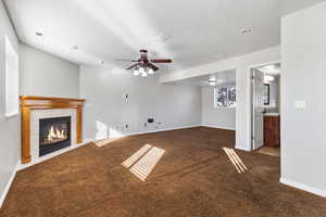 Unfurnished living room with dark carpet, a fireplace, a ceiling fan, and a textured ceiling