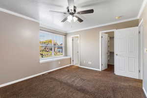 Unfurnished bedroom with a textured ceiling, crown molding, dark colored carpet, a walk in closet, and a ceiling fan