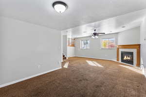 Unfurnished living room featuring carpet flooring, a fireplace, a textured ceiling, stairs, and ceiling fan