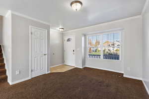 Carpeted entryway with ornamental molding and baseboards