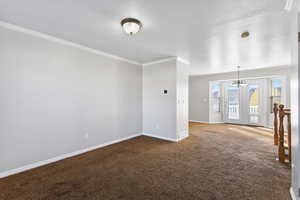 Carpeted empty room with a chandelier, crown molding, and a textured ceiling