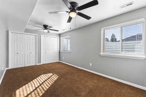 Unfurnished bedroom with two closets, carpet, ceiling fan, and a textured ceiling