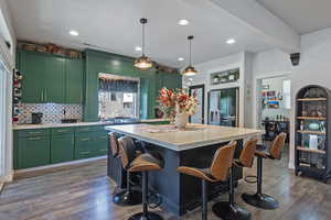 Kitchen featuring green cabinetry, dark wood-style flooring, decorative light fixtures, a breakfast bar area, and decorative backsplash