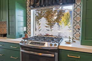 Kitchen with green cabinets, stainless steel range with gas stovetop, and light stone counters