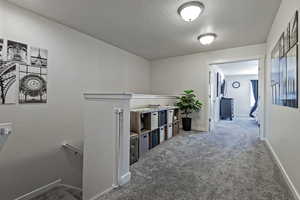 Hallway with an upstairs landing, carpet, and a textured ceiling