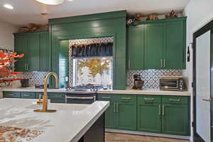 Kitchen featuring green cabinets, decorative backsplash, stainless steel gas range oven, light wood-style flooring, and recessed lighting