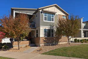 View of front of house featuring a balcony, brick siding, and a front lawn