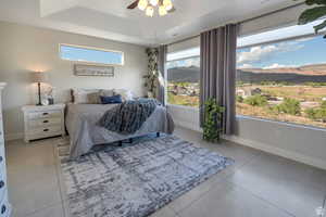 Bedroom featuring a mountain view, a raised ceiling, light tile patterned floors, and ceiling fan