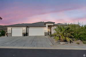 View of front of house featuring a garage, concrete driveway, stucco siding, a tiled roof, and stone siding