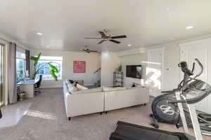 Carpeted living room with ceiling fan, recessed lighting, and stairs