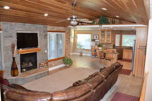 Living area featuring light tile patterned flooring, healthy amount of natural light, a stone fireplace, lofted ceiling, and ceiling fan