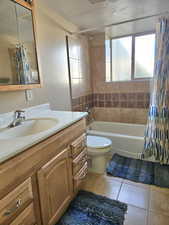 Bathroom featuring a textured ceiling, light tile patterned floors, shower / bath combination with curtain, and vanity
