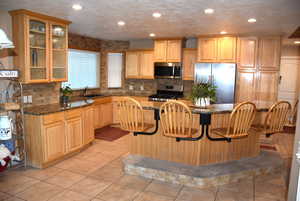 Kitchen with a breakfast bar area, appliances with stainless steel finishes, light tile patterned floors, a center island, and a textured ceiling